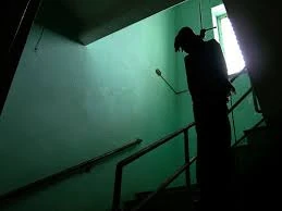 Silueta de una persona en una escalera con paredes verdes, creando un ambiente misterioso y sombrío.