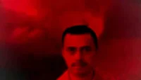 Retrato de un hombre con fondo rojo, mostrando una expresión seria y un bigote, en un ambiente dramático y evocador.
