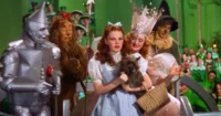 Dorothy, personaje principal de "El Mago de Oz", sostiene a su perro mientras está rodeada por el Espantapájaros, el León Cobarde y la Buena Bruja del Norte, en una escena icónica de la película clásica.