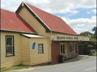 Tienda general Masons, edificio de madera con techo rojo, ubicada en una calle rural. Ideal para artículos locales y productos esenciales.